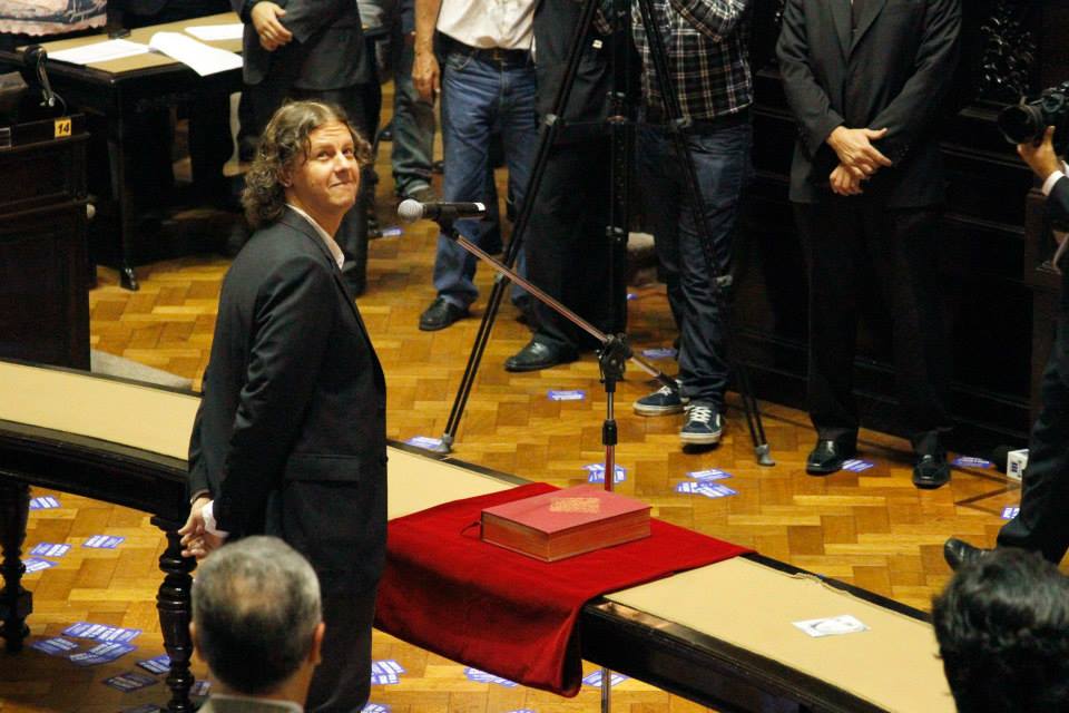 Tras asumir en la Lesgislatura de la provincia de Buenos Aires, Christian Castillo saluda con el puño en alto al palco en el cual se encuentran sus compañeros de militancia